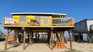 Una struttura in legno con un edificio blu e giallo su palafitte, una panchina di legno e un tavolo da picnic.