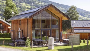 A wooden lodge with a large glass entrance, outdoor seating, and a mountain backdrop. - Amazing Chalet With Whirlpool (Sankt Georgen am Kreischberg)