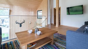 A modern living room with wooden walls and a sloped ceiling, a wooden coffee table with cups and a kettle, a blue sofa, and a flat-screen TV mounted on the wall. - Amazing Chalet With Whirlpool (Sankt Georgen am Kreischberg)