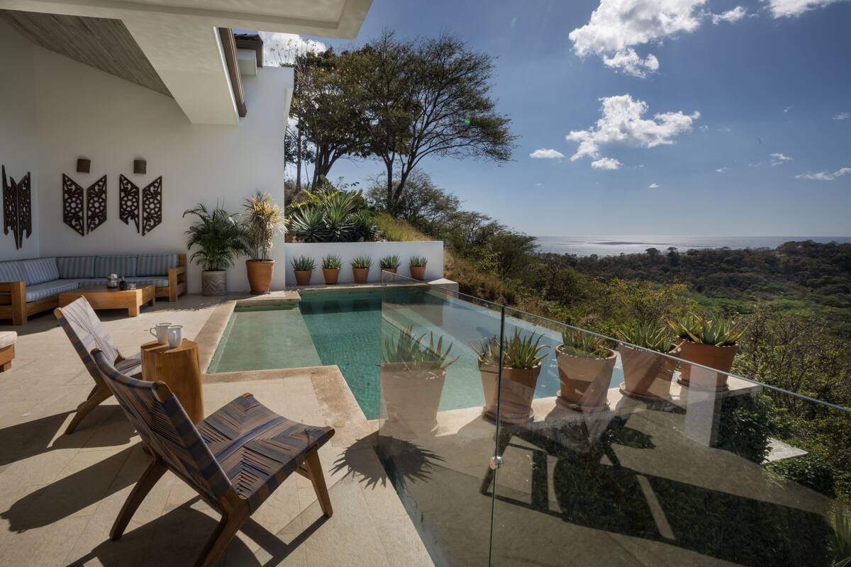 A modern outdoor pool area with lounge chairs, potted plants, and a view of the landscape.
