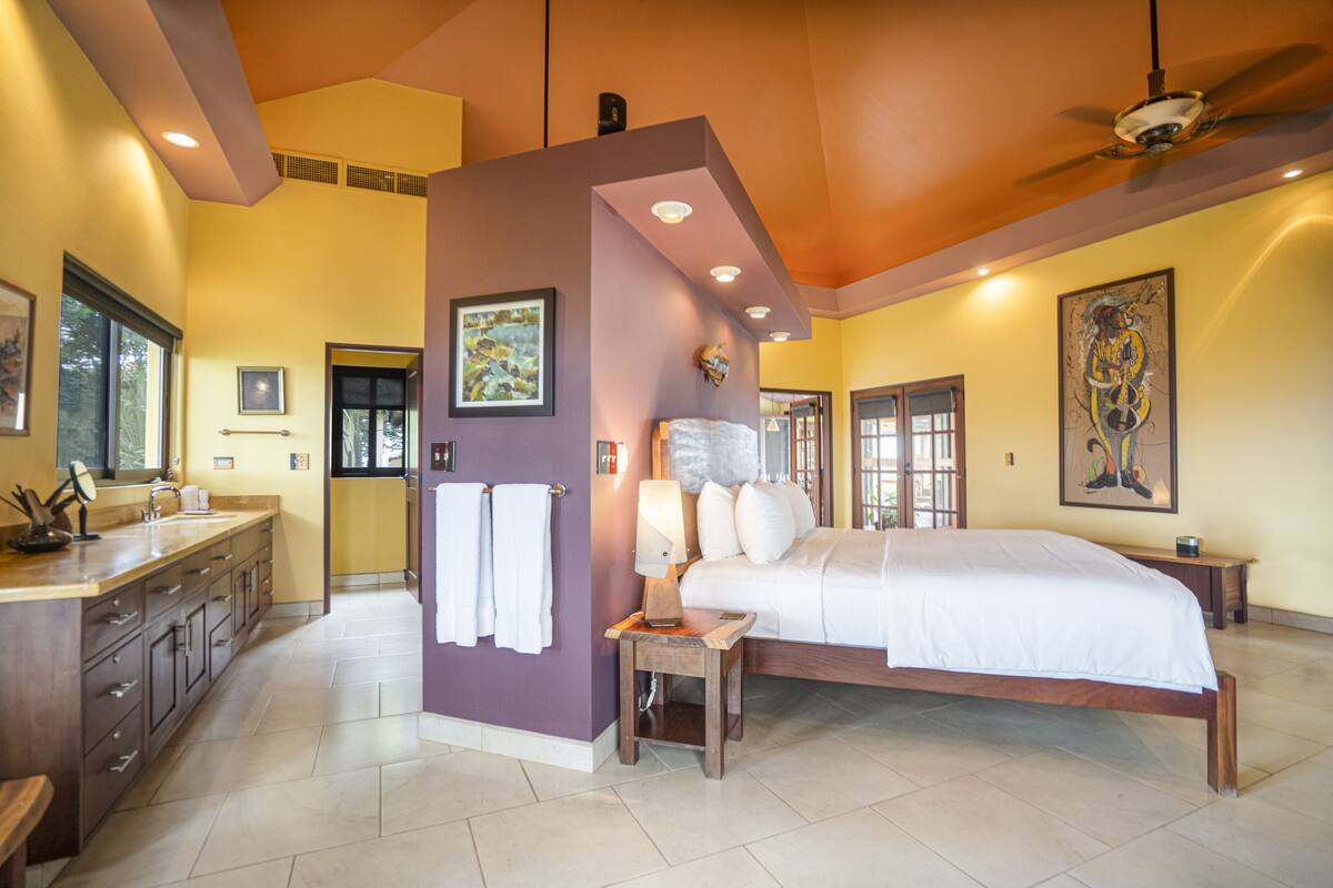 A bedroom with a large bed, a nightstand, a wall-mounted lamp, and a ceiling fan.