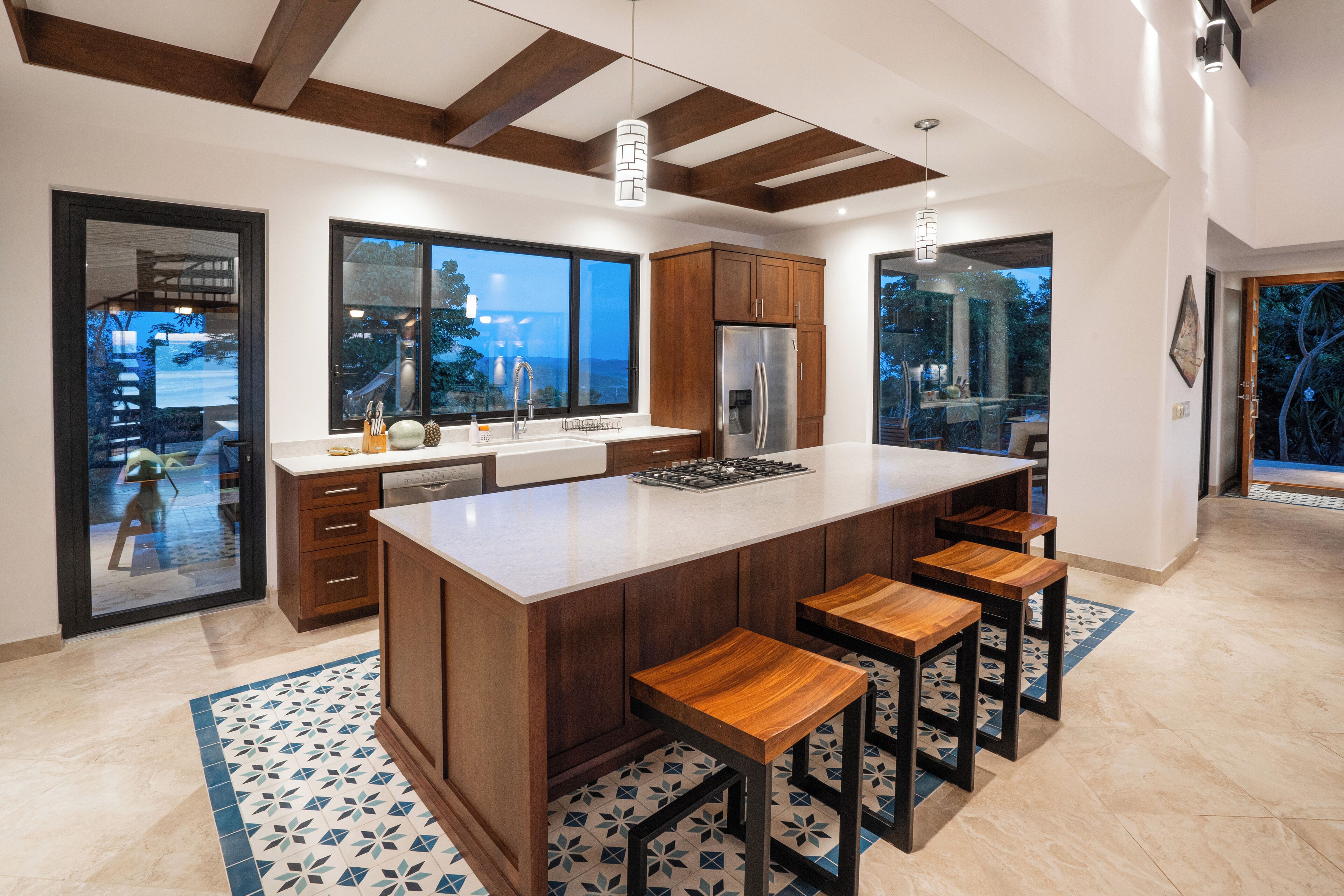 A modern kitchen with a large island, wooden bar stools, and a view of the outdoors.