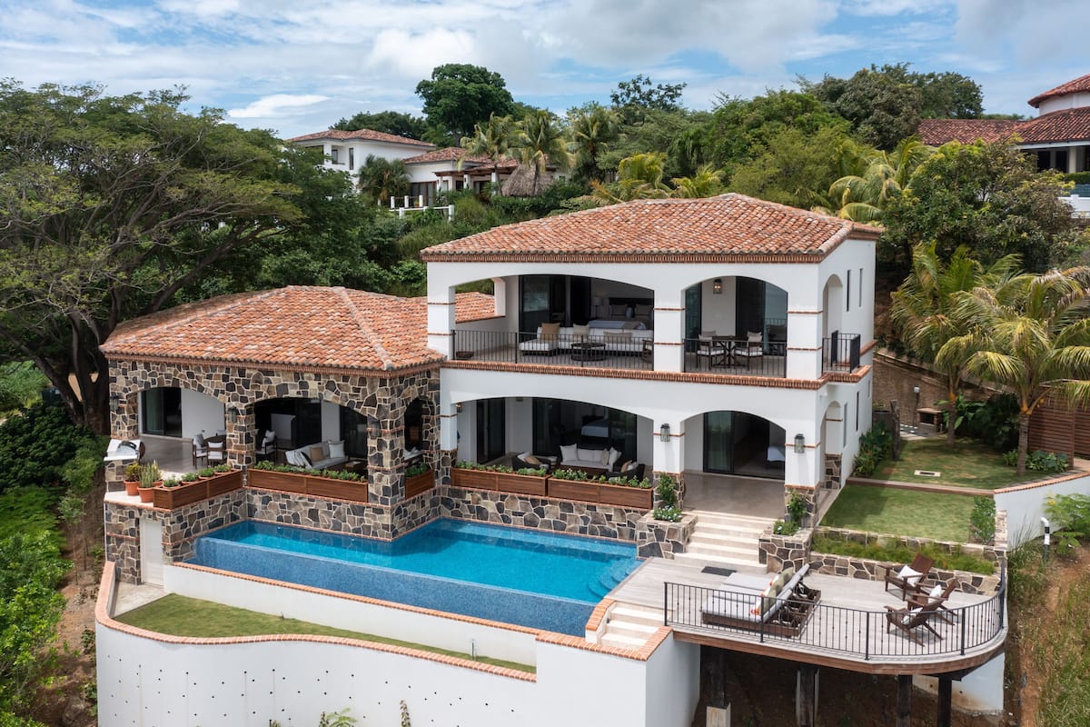 A two-story house with a swimming pool, outdoor seating, and a garden.