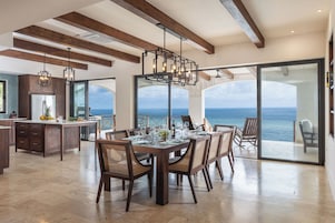Un comedor espacioso con una mesa grande, sillas de madera y vista al océano.