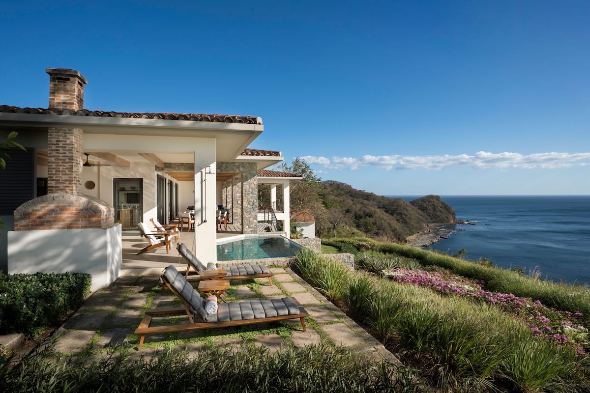 A coastal house with a swimming pool, outdoor seating, and a view of the ocean.