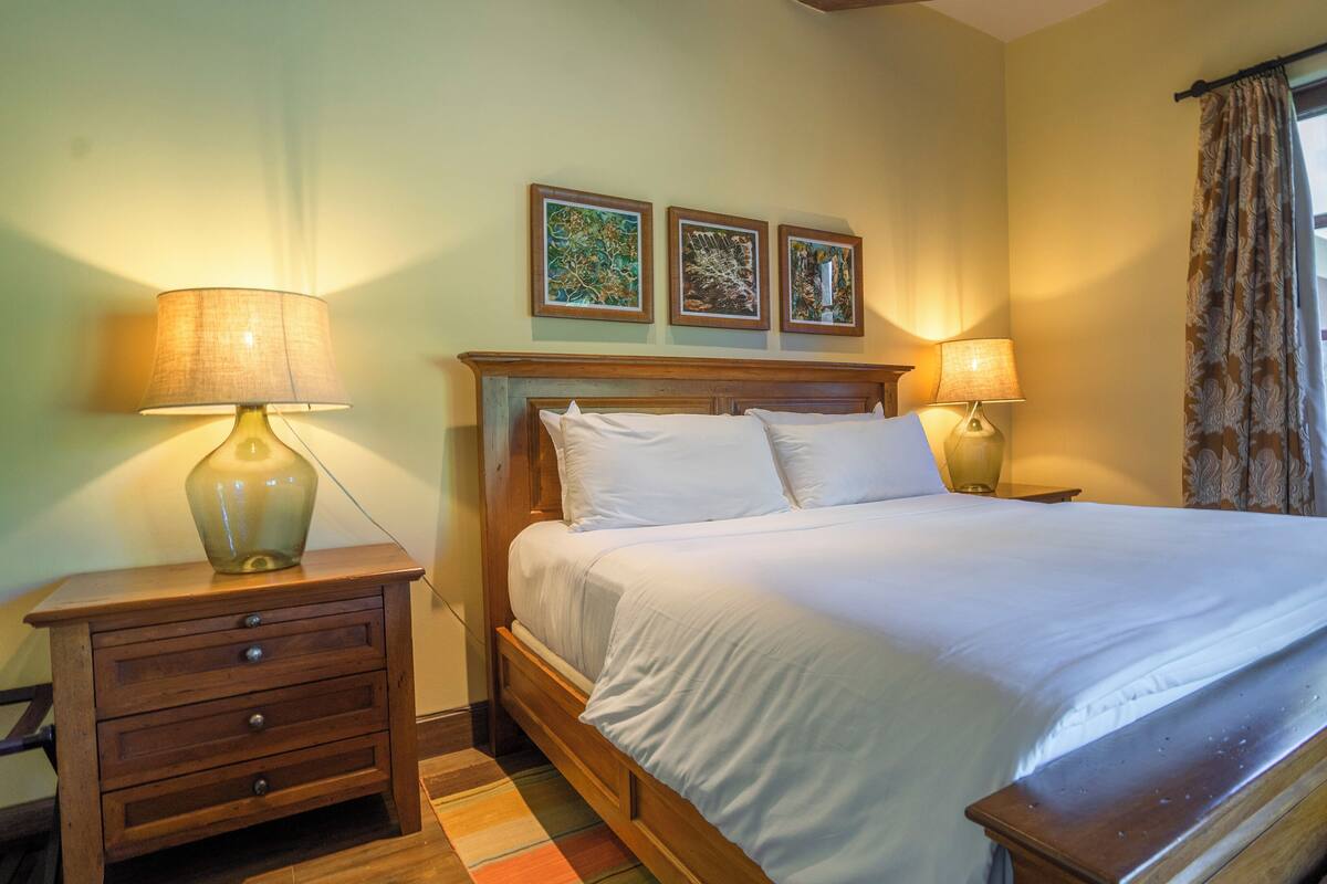 A neatly made bed with white linens, two bedside tables with lamps, and three framed pictures on the wall.