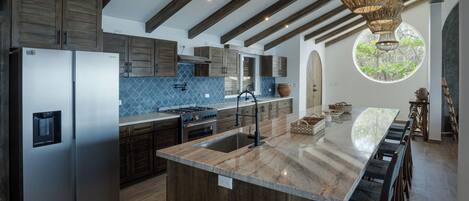 A modern kitchen with a large island, stainless steel appliances, and a view of greenery through a circular window.