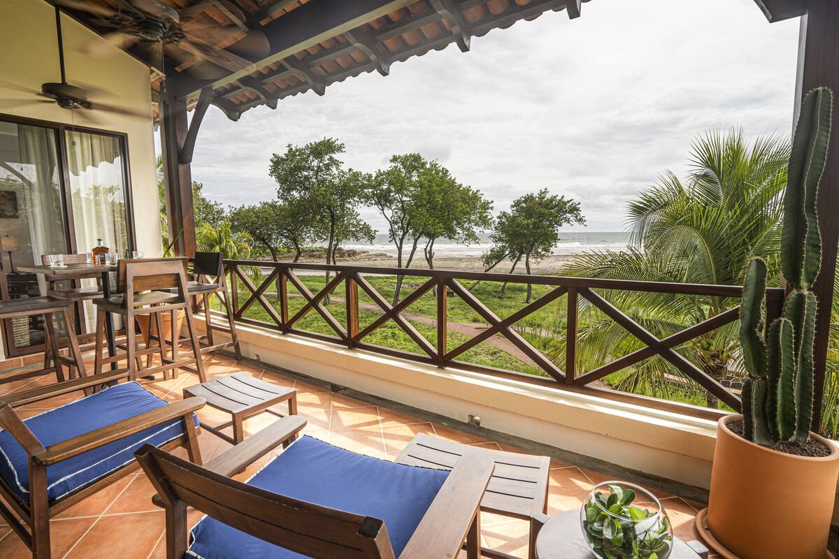 A terrace with wooden furniture, a cactus, and a view of the beach.