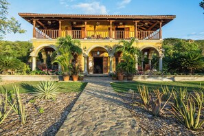 A two-story building with a balcony, arched walkways, and potted plants. - Rancho Santana (Tola)