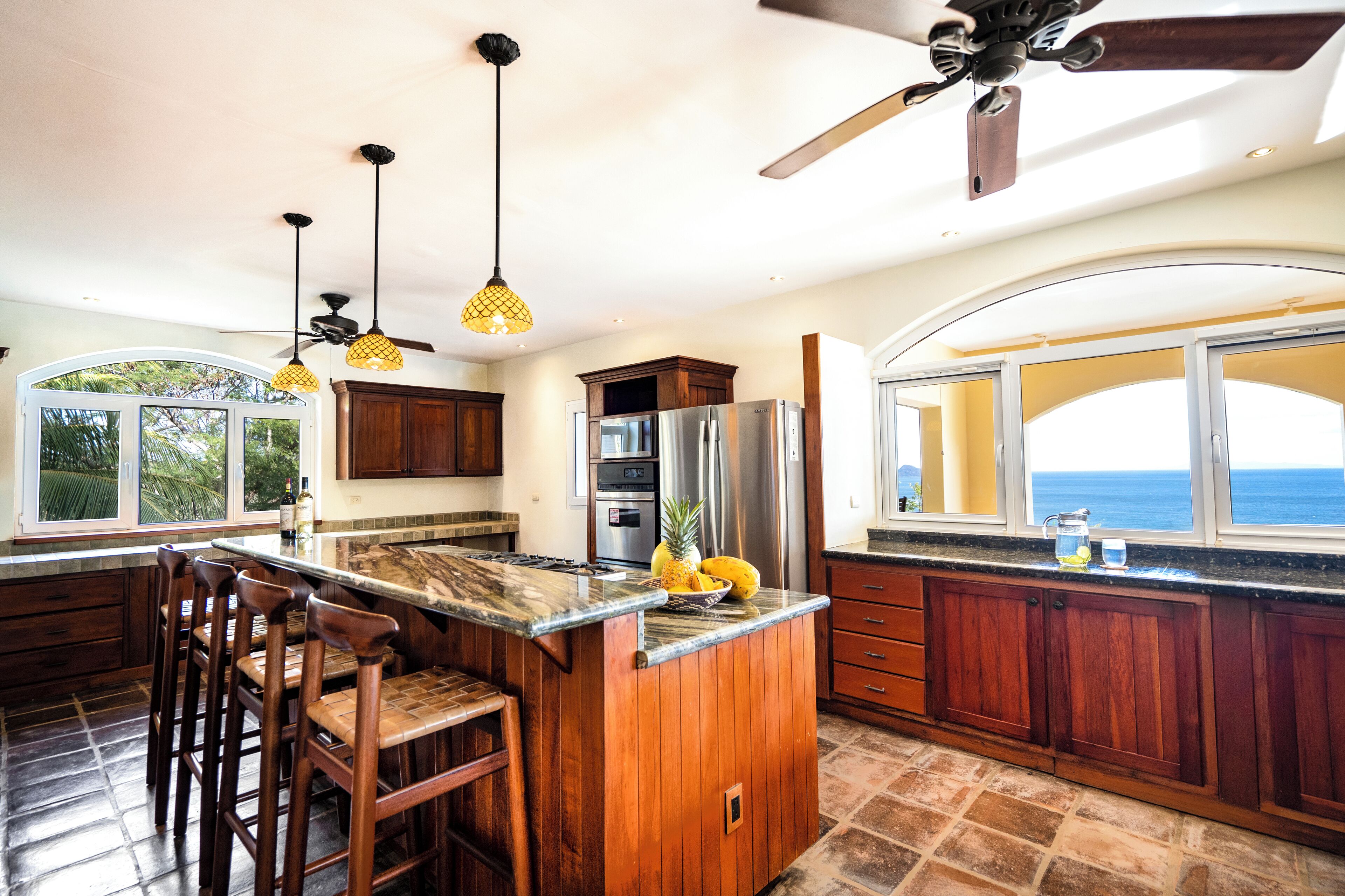 Una cocina con una isla grande, armarios de madera y vista al océano.