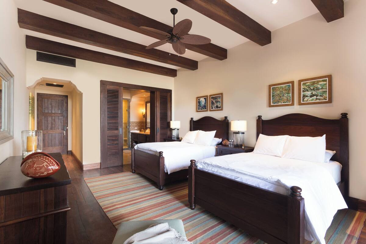 A hotel room with two wooden beds, a ceiling fan, and a large window.