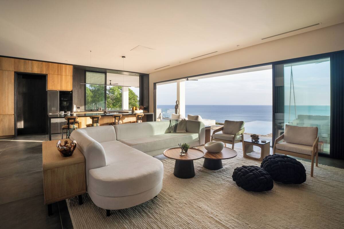 A modern living room with a large window, a sofa, a coffee table, and a dining area.