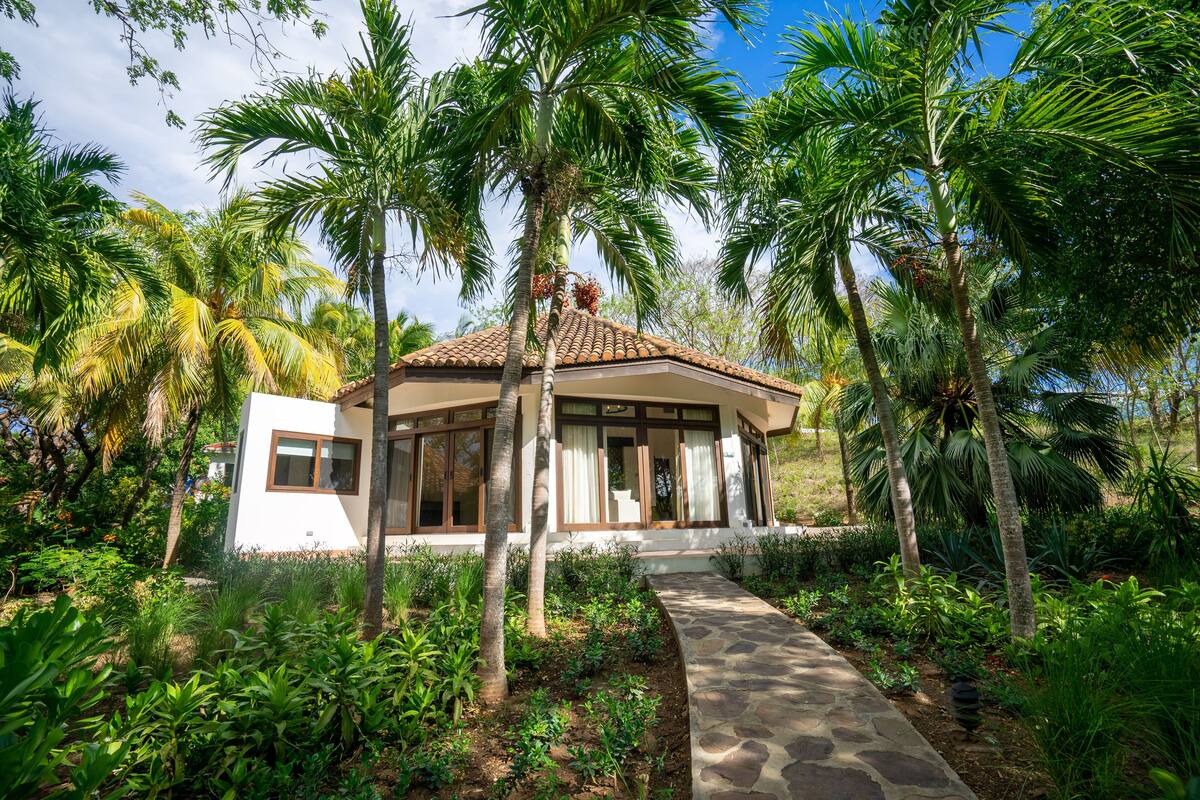 A house with a tiled roof, surrounded by lush greenery and palm trees.