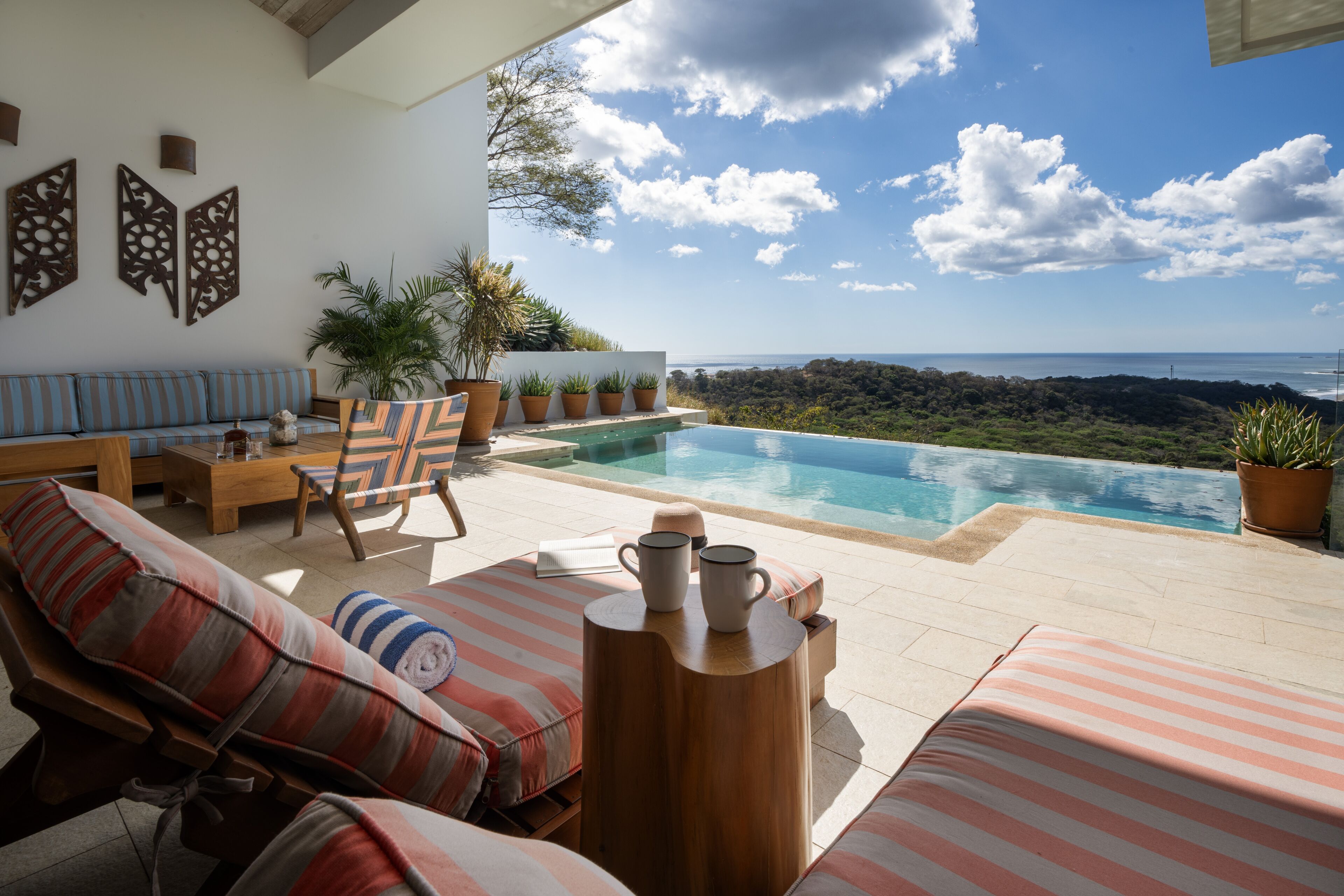 A poolside area with lounge chairs, a wooden table, and potted plants.
