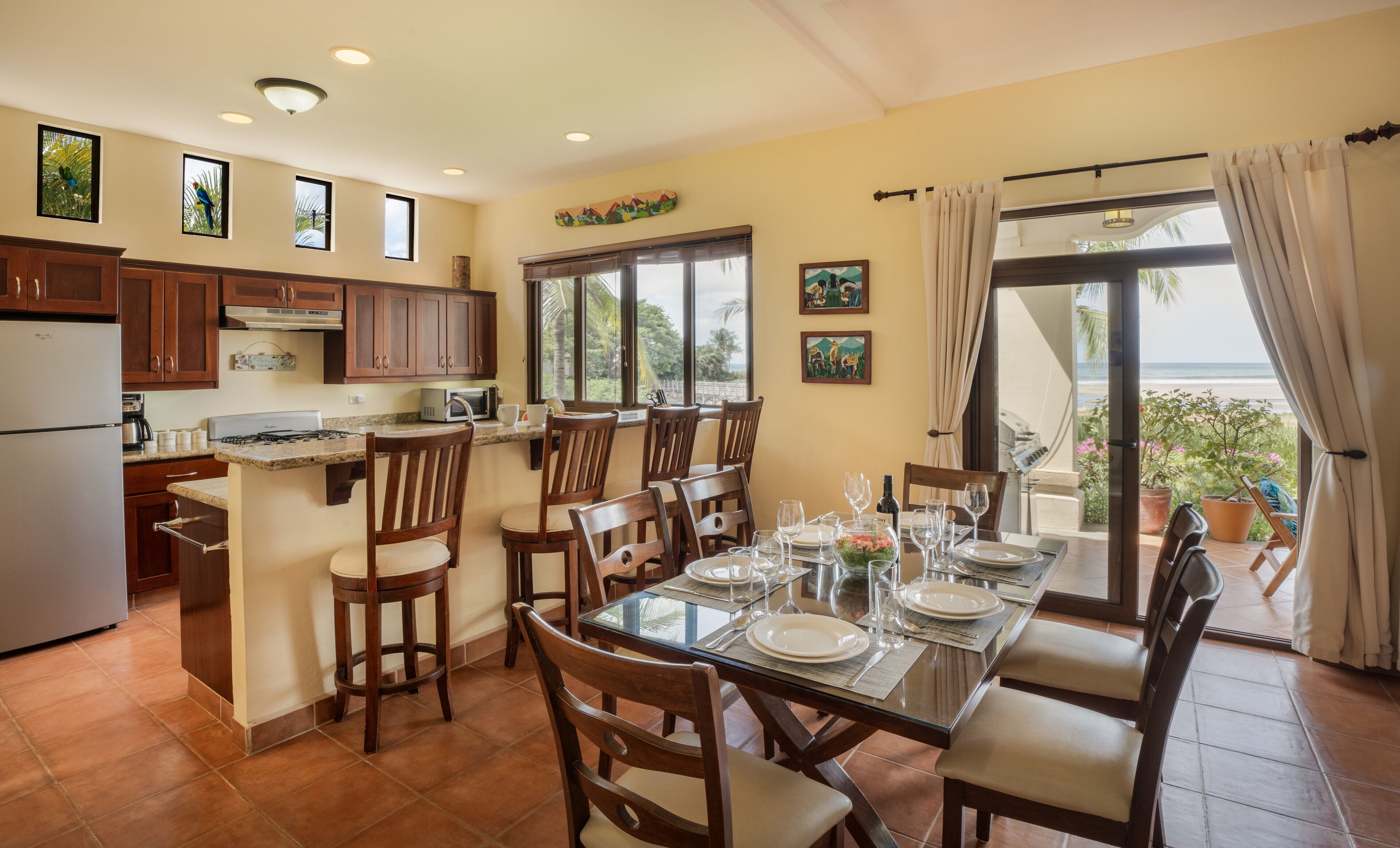 A dining area with a glass table, chairs, and a view of the beach.
