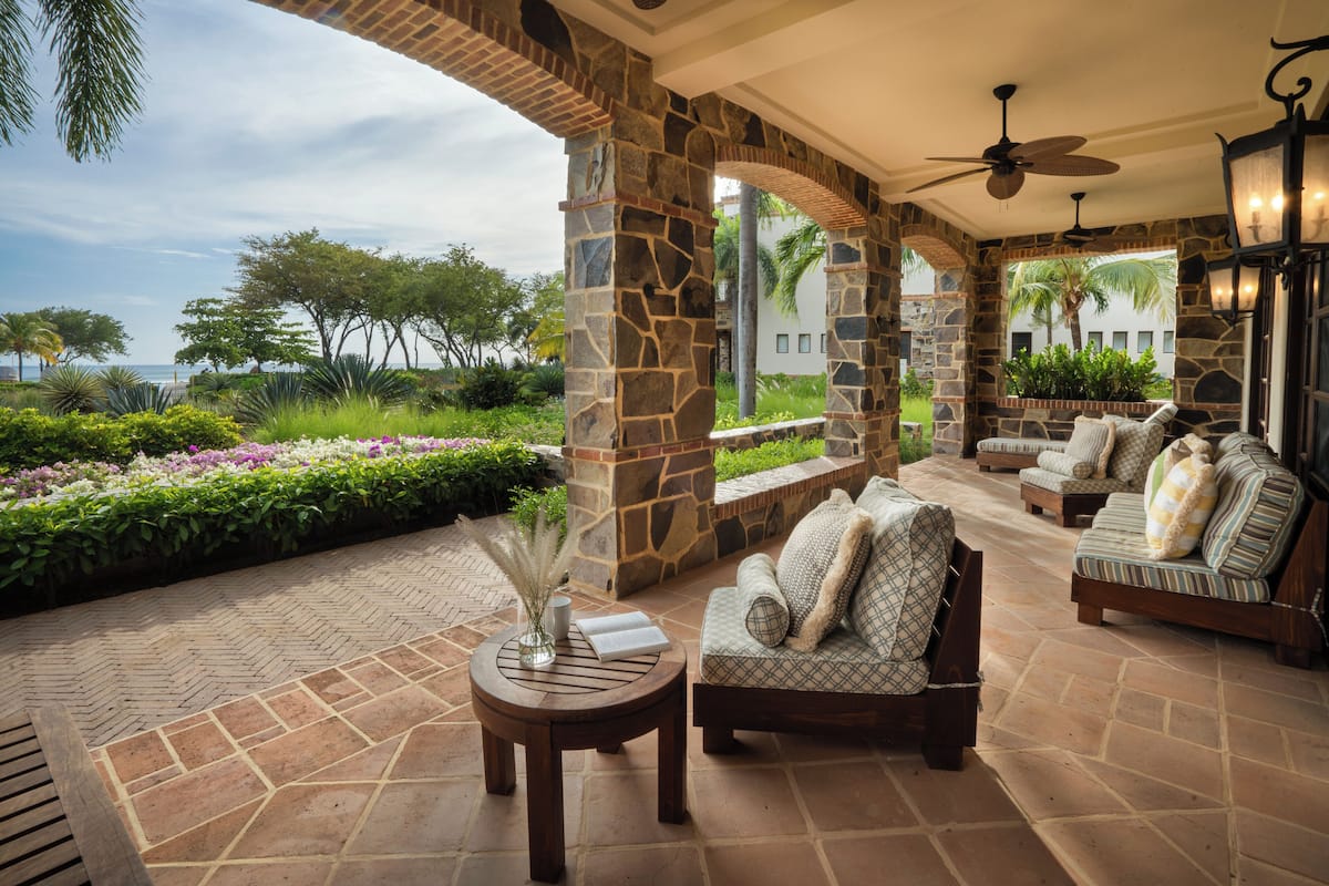 A covered outdoor seating area with stone pillars, a ceiling fan, and a view of the ocean.
