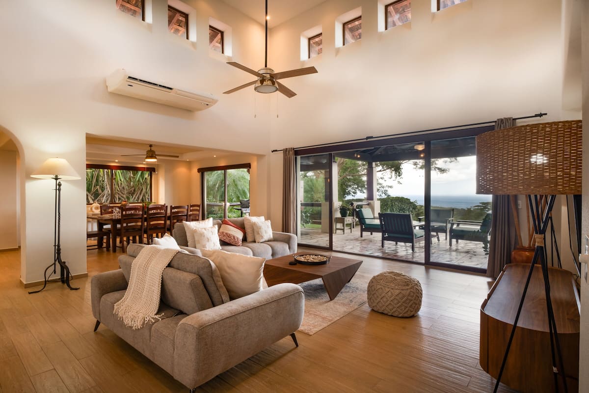 A spacious living room with a ceiling fan, a dining area with a table and chairs, and a large sliding glass door leading to an outdoor patio.
