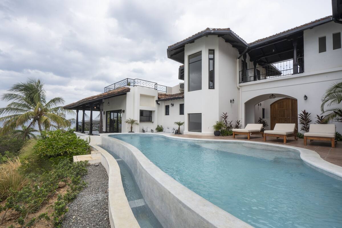 A modern pool area with a curved pool, lounge chairs, and a two-story building with balconies.