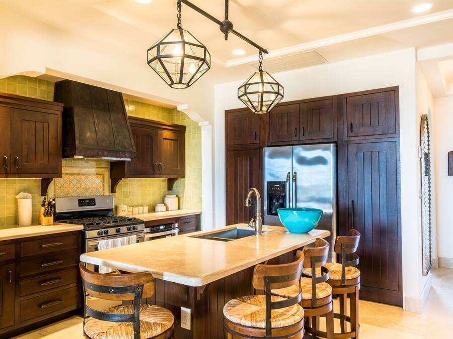 Une cuisine moderne avec des meubles en bois foncé, un grand îlot central doté de tabourets, des appareils en acier inoxydable et un éclairage suspendu.