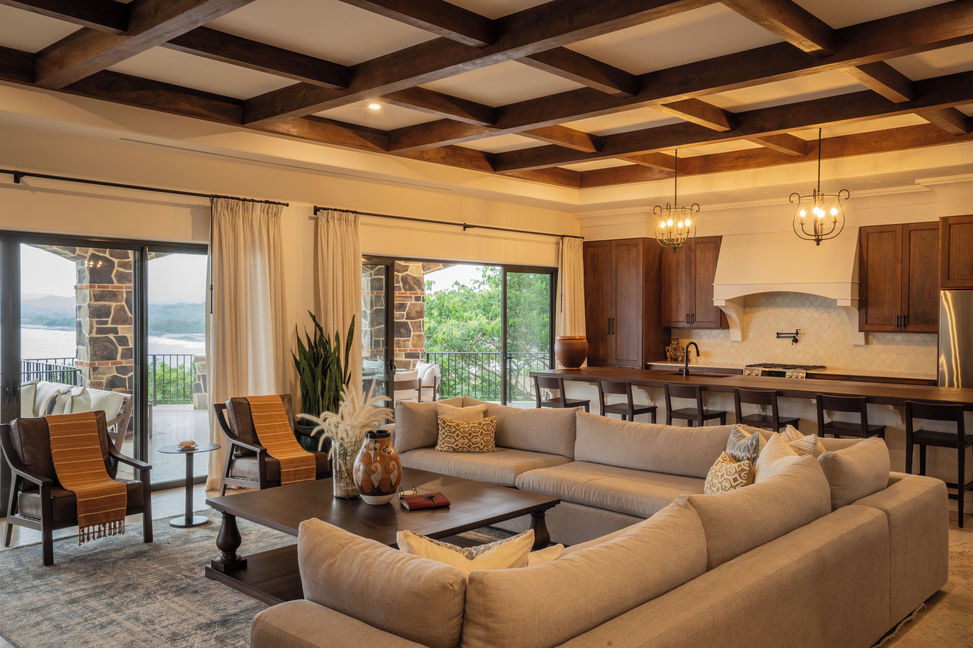 Un salón amplio con un sofá grande, una mesa de centro y una zona de comedor con sillas de madera, y una cocina al fondo.