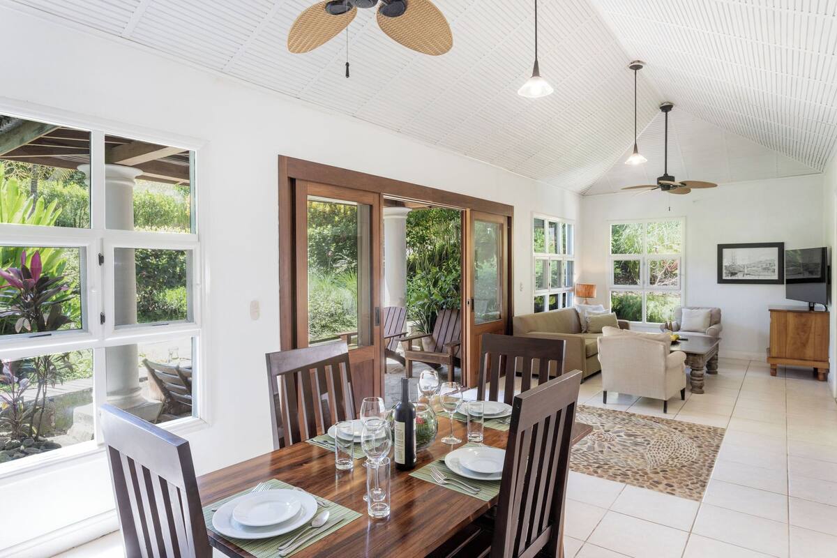 A spacious dining area with a wooden table set for six, large windows, and a ceiling fan.