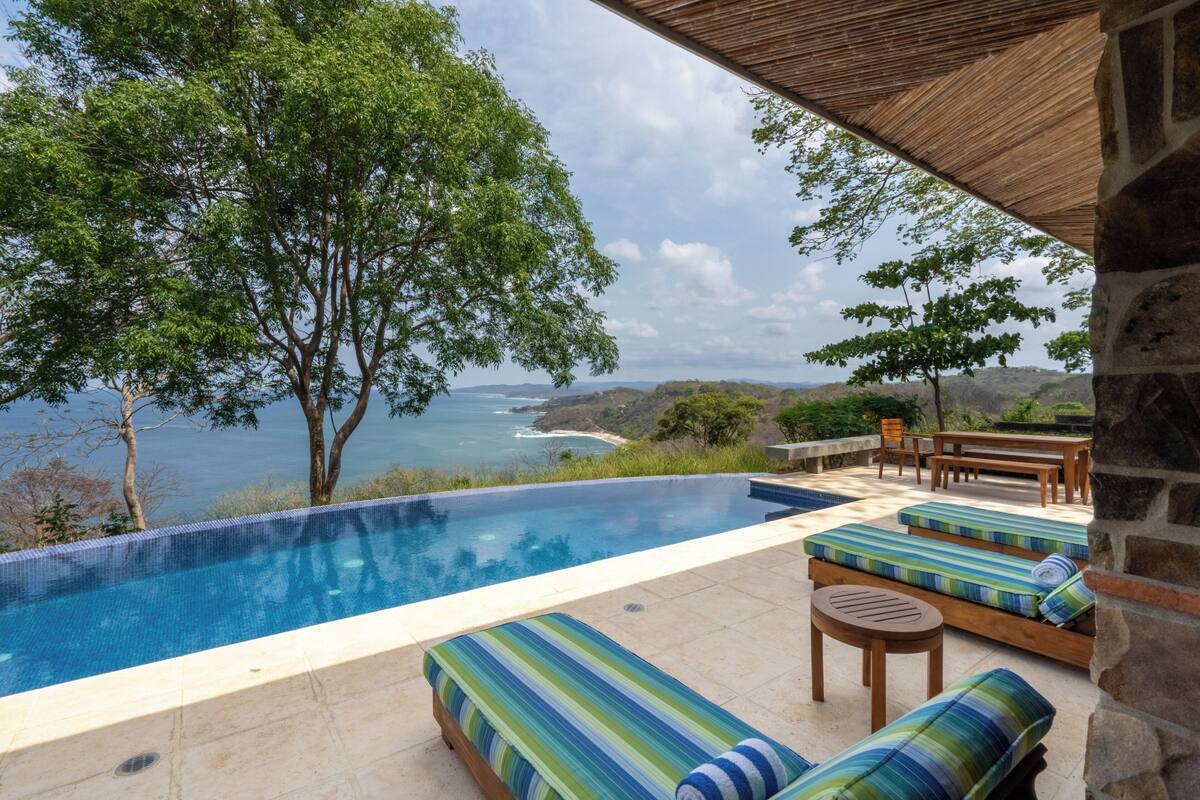 A pool with lounge chairs and a view of the sea.