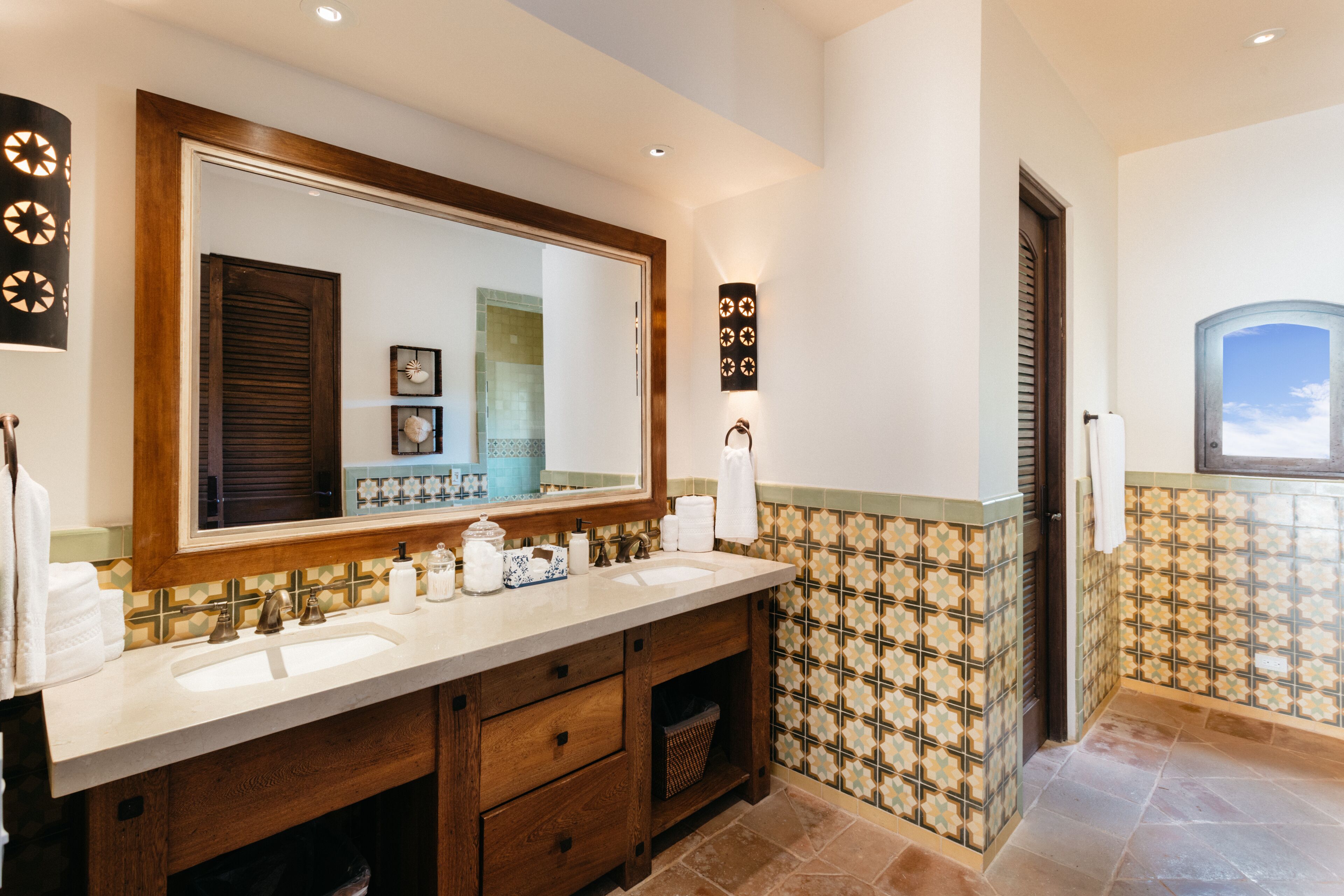 A bathroom with a large mirror, wooden vanity, multiple sinks, and decorative wall tiles.
