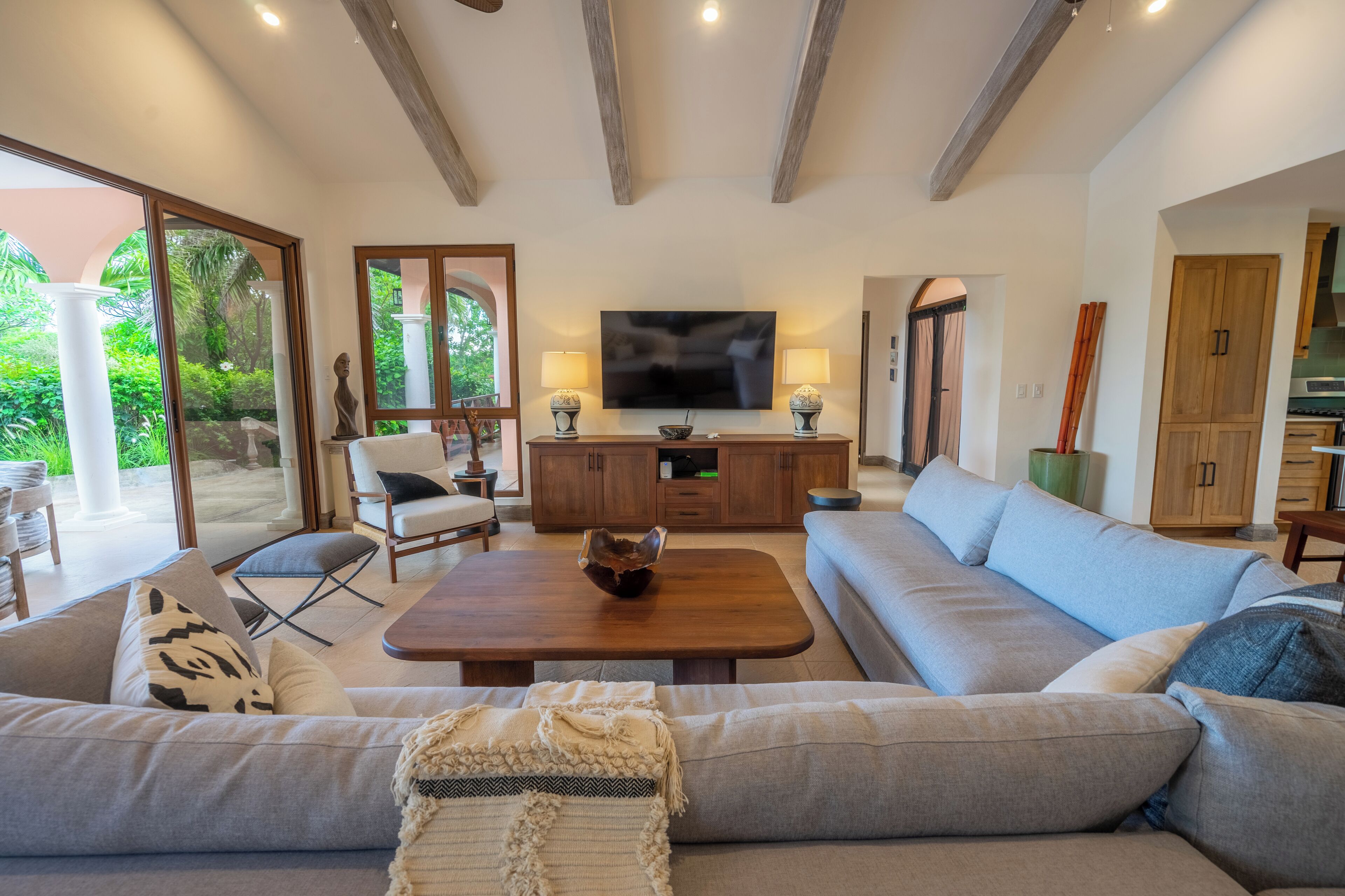 Amplia sala de estar con un sofá grande, una mesa de centro y un televisor. Se ve un aparador de madera y un comedor al fondo.