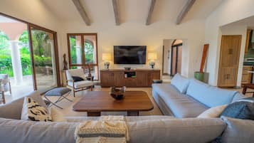 Amplia sala de estar con un sofá grande, una mesa de centro y un televisor. Se ve un aparador de madera y un comedor al fondo.