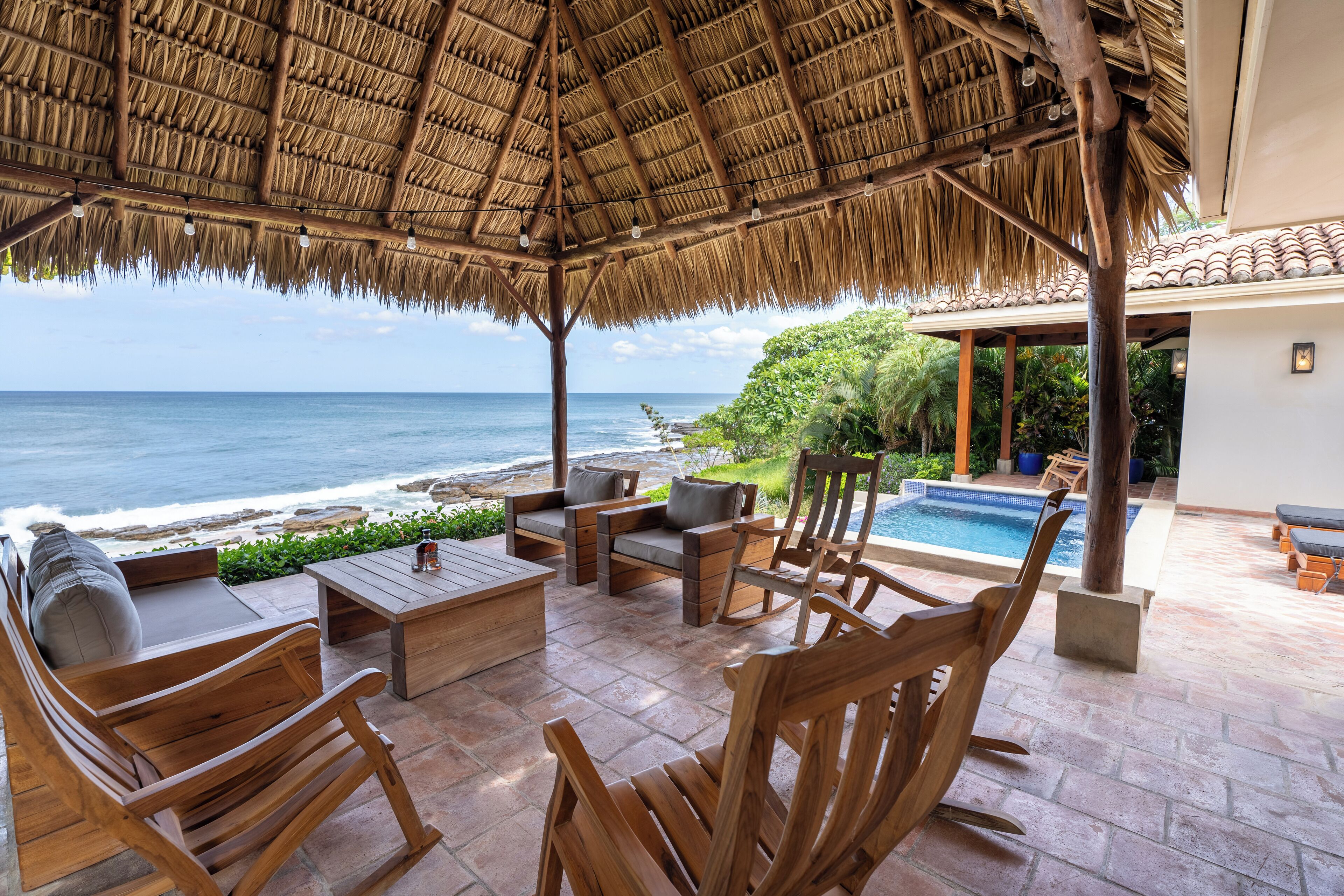 A wooden outdoor seating area with a thatched roof overlooking the ocean.