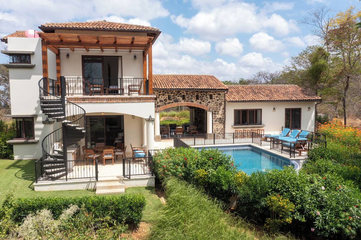 A two-story house with a swimming pool, outdoor seating, and a stone archway.