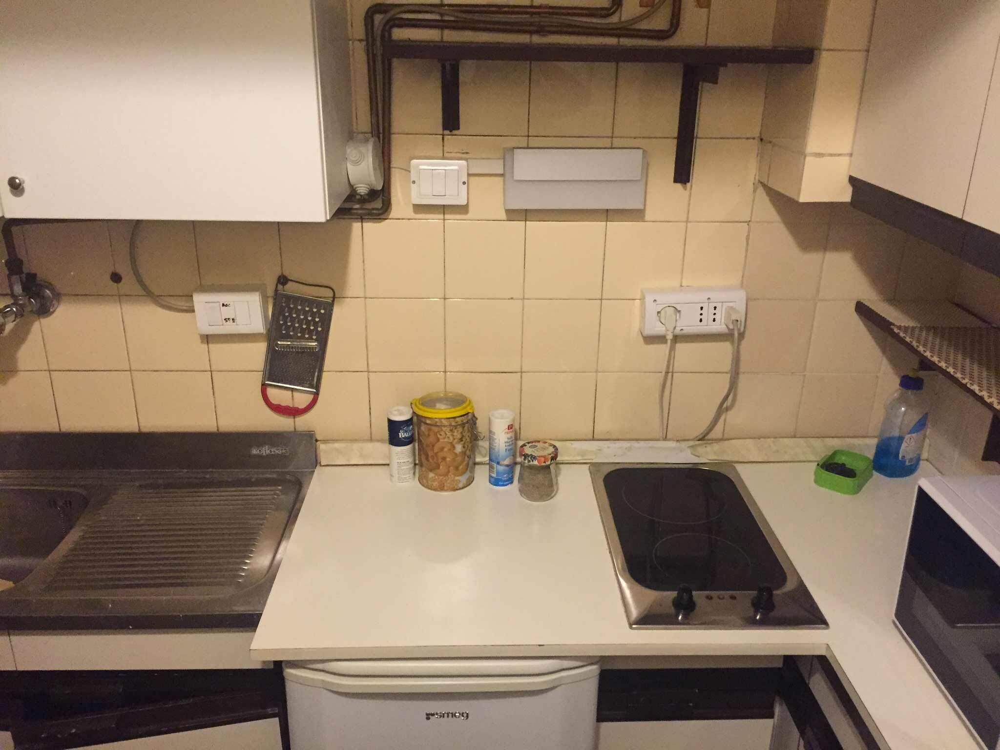 Une cuisine équipée d’une cuisinière, d’un évier et d’un petit réfrigérateur. On y trouve divers ustensiles de cuisine sur le plan de travail, notamment des bocaux et une bouteille.