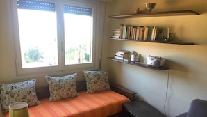 A cozy room with a sofa, a table with a lamp, a bookshelf, and a window with blinds. - Eurotel 312 (Rapallo)