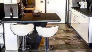 A modern kitchen with a central island, two bar stools, a refrigerator, and a microwave.