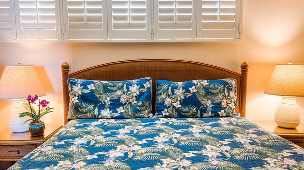 A bed with a floral bedspread, two matching pillows, a wooden headboard, and two bedside lamps with a potted plant on each side.