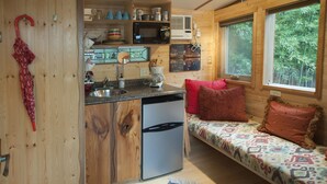 A compact kitchen with a sink, refrigerator, and microwave. There's a small dining area with a bench and pillows. - The Tiny House in Travis Heights (Austin)