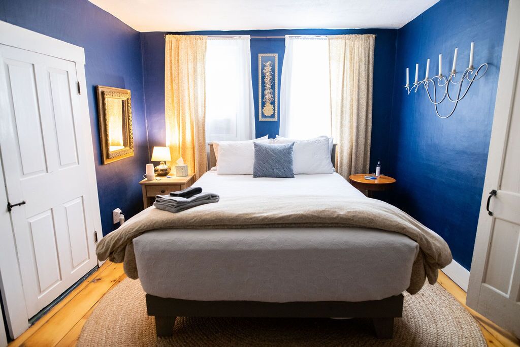 A bedroom with a bed, a nightstand, a lamp, a wall-mounted candelabra, and a door.