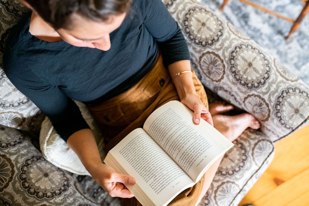 A person sitting on a patterned couch, reading a book.