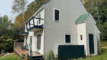 Charming two-story house with a front porch and green door, surrounded by a wooded area.