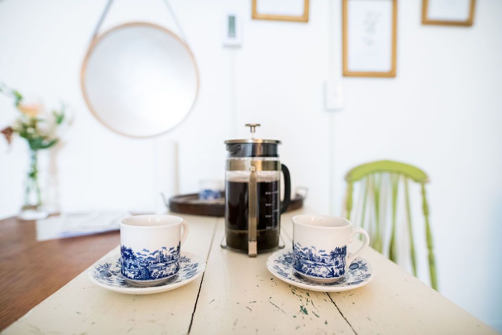 Una mesa de madera con dos tazas blancas decoradas con diseños azules y una cafetera.