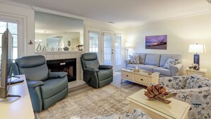Una sala de estar con chimenea, dos sillones de cuero, un sofá, una mesa de centro y una mesita auxiliar con lámpara.