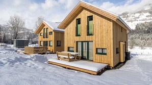 A wooden cabin with a snow-covered deck and a bench, surrounded by a snowy landscape and mountains. - Nice Chalet With Whirlpool (Sankt Georgen am Kreischberg)