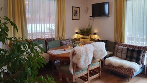 A cozy living room with a wooden dining table, two sofas, and a television mounted on the wall.