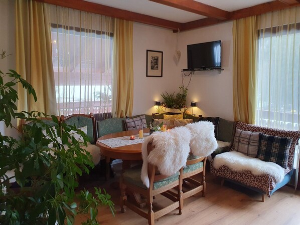 Uma sala de estar acolhedora com uma mesa de jantar de madeira, dois sofás e uma televisão fixada na parede.
