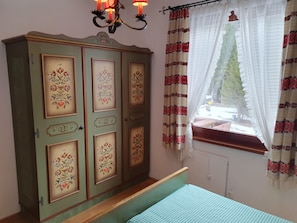 A bedroom with a bed, a wardrobe with floral designs, a chandelier, and a window with curtains.