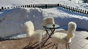 A snow-covered outdoor seating area with a table and chairs, surrounded by a wooden fence and snowbanks.