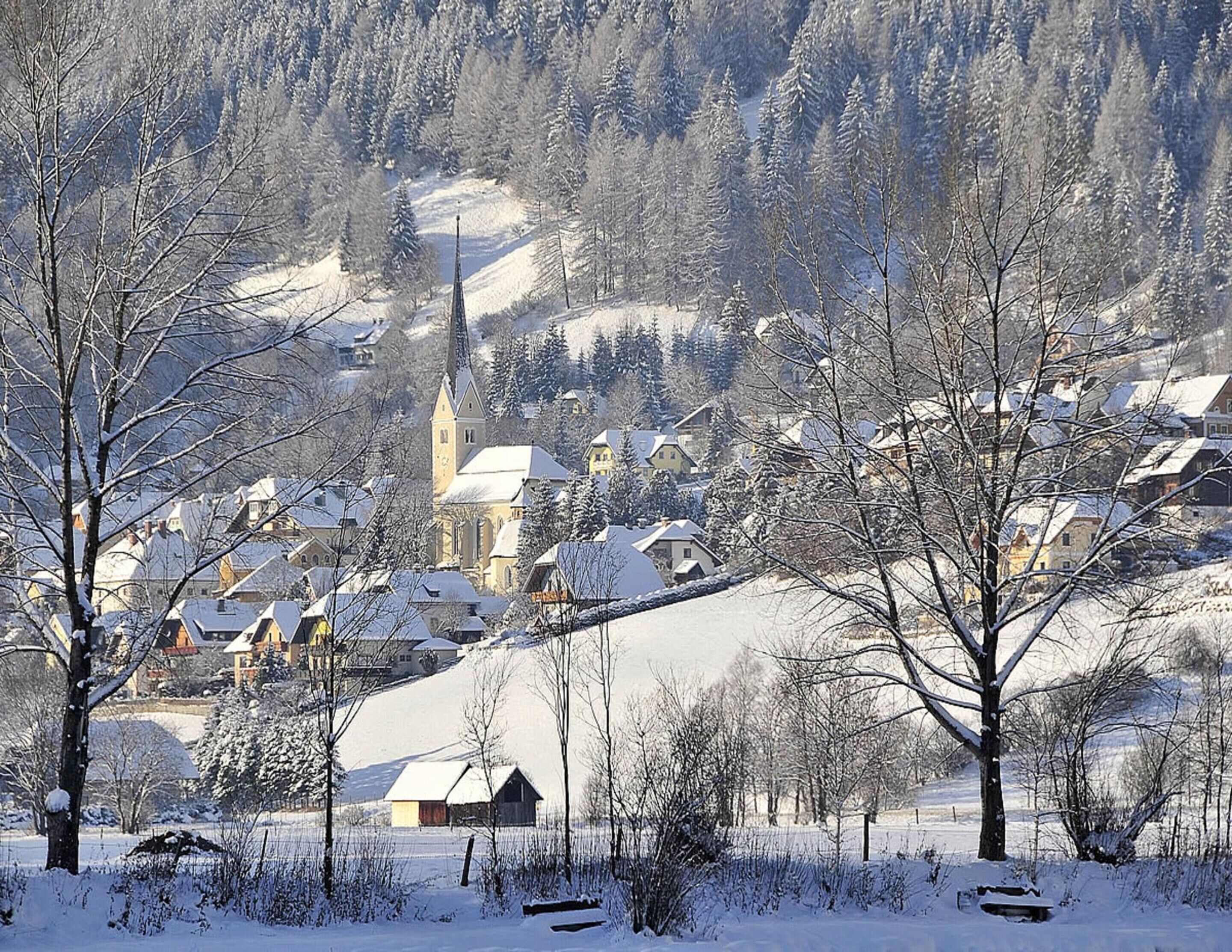 A snow-covered village with traditional houses, a church, and a prominent tower.