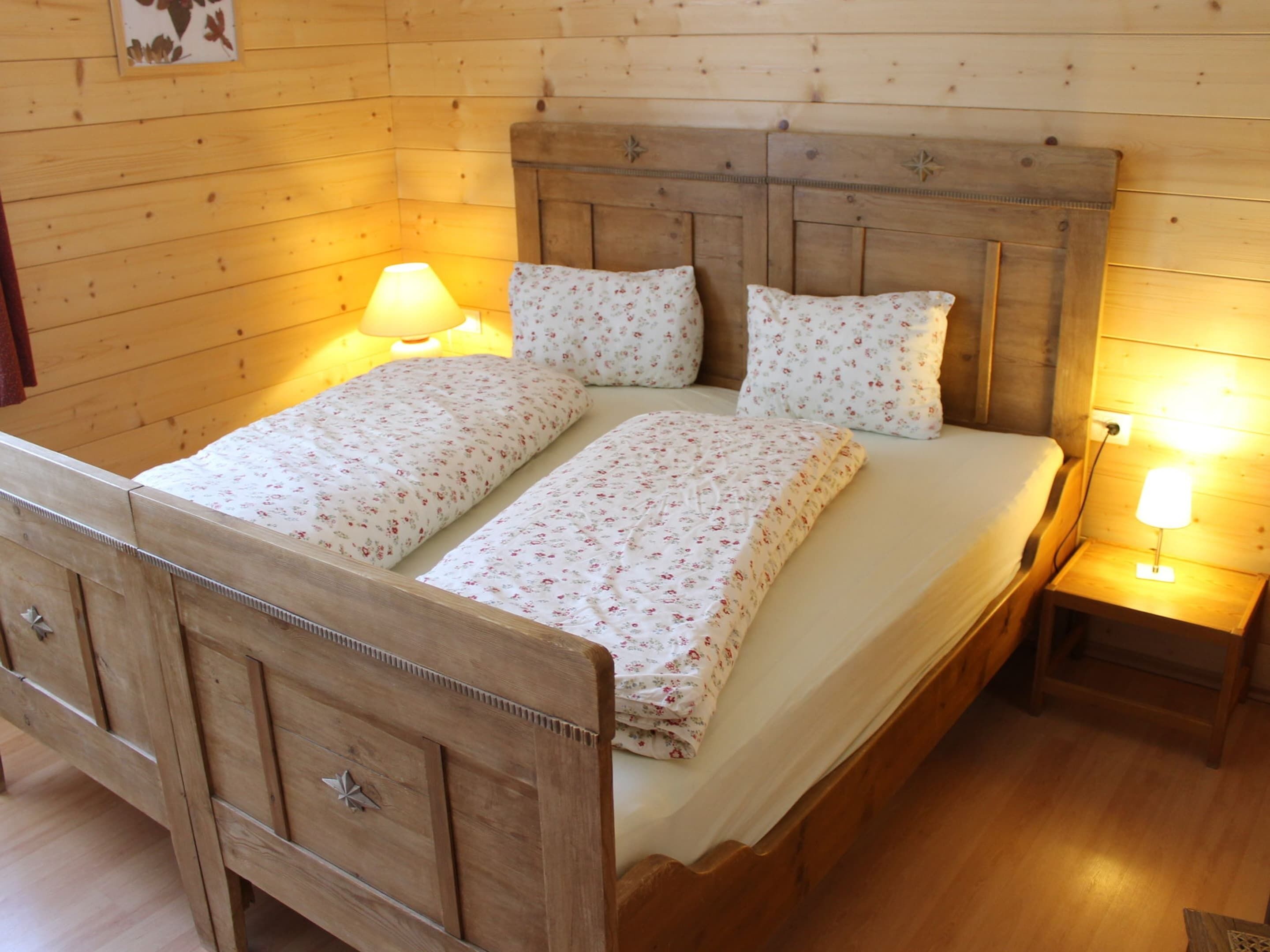 A wooden bed with floral bedding, two bedside lamps, and a nightstand.