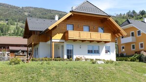 A two-story wooden house with a balcony, a front porch, and a view of a forested hillside. - Huge Apartment in Sankt Margarethen im Lungau near Ski Lift (Sankt Michael im Lungau)