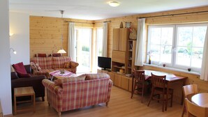 A cozy living room with a plaid sofa, a small table, and a television. There is a wooden dining table with chairs and a window with curtains. - Huge Apartment in Sankt Margarethen im Lungau near Ski Lift (Sankt Michael im Lungau)